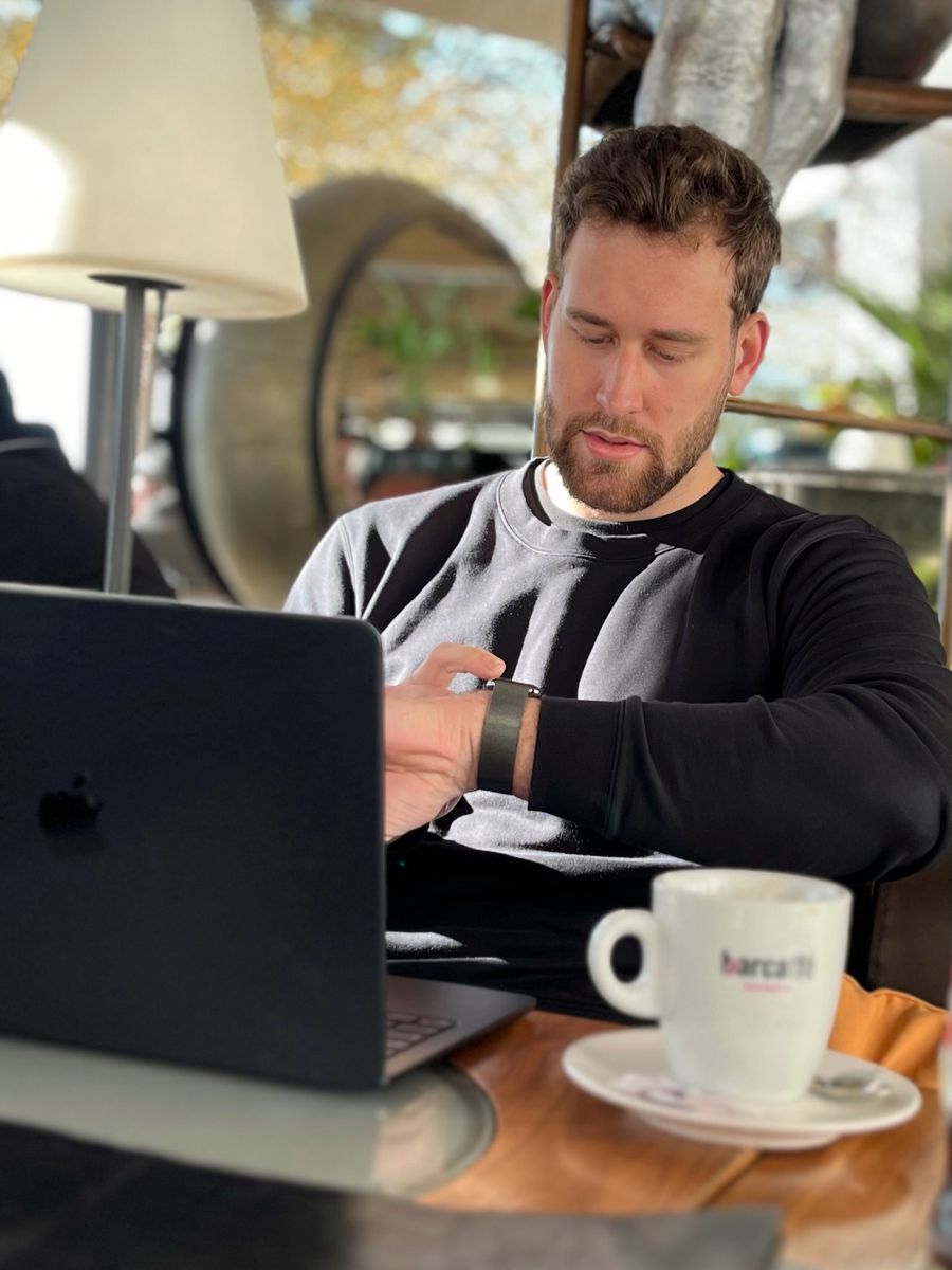 Robi nel 2024, al tavolino di un bar con il portatile e un caffè, mentre guarda l'orologio